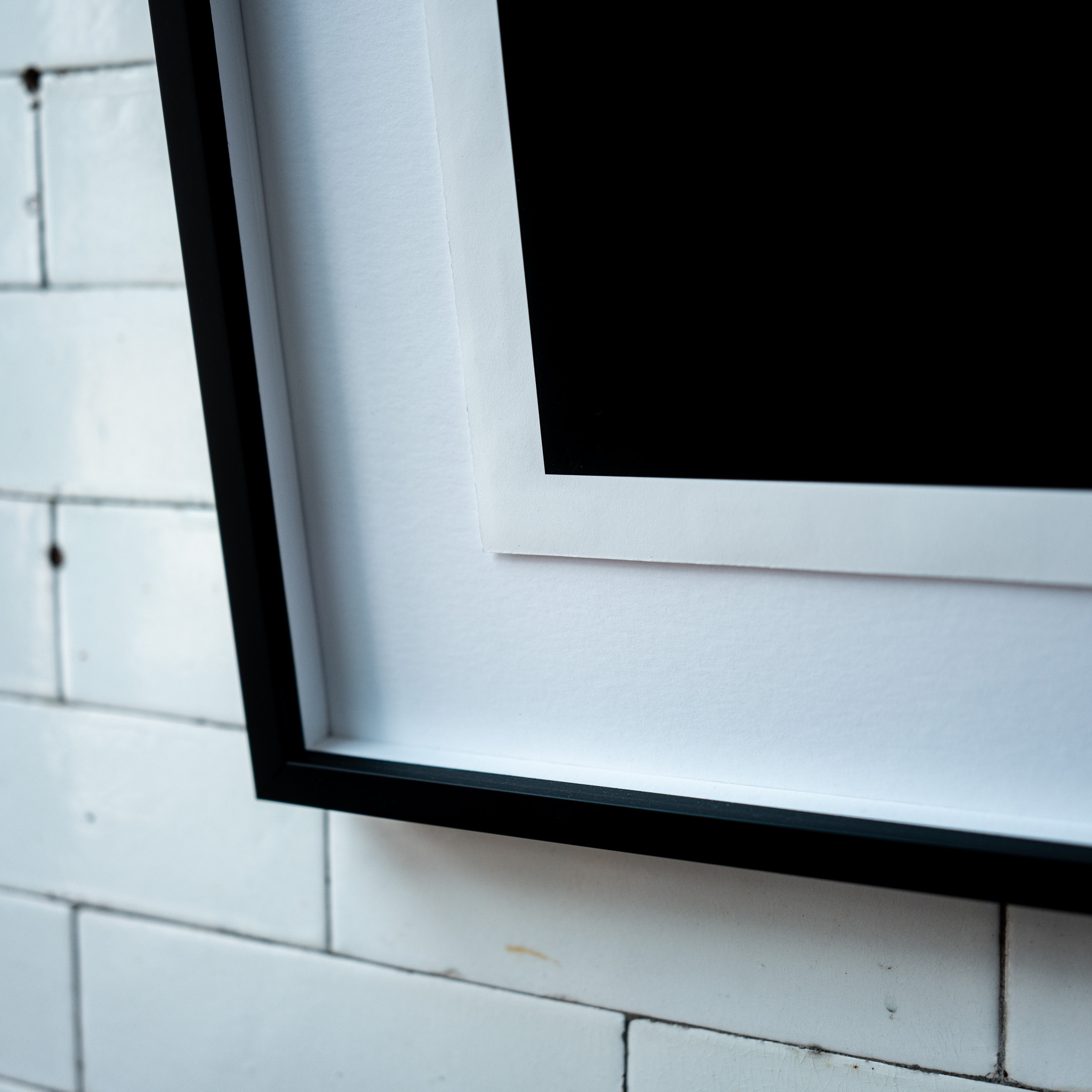 Corner detail of a framed archival print showing the white mount border and black moulding